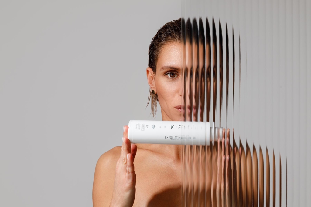 Naked woman behind the textured glass showing the skincare product. 